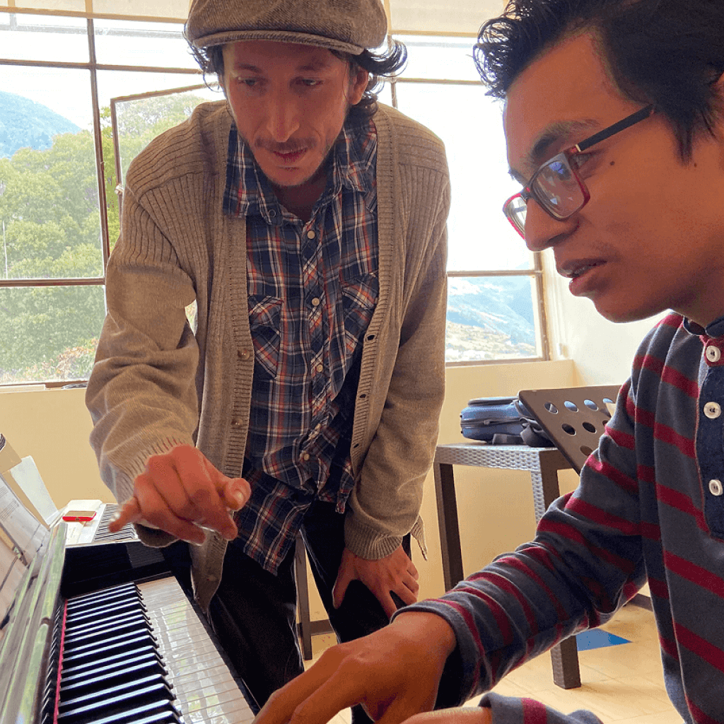 Docente enseñando a estudiante sobre clases de piano de forma práctica.