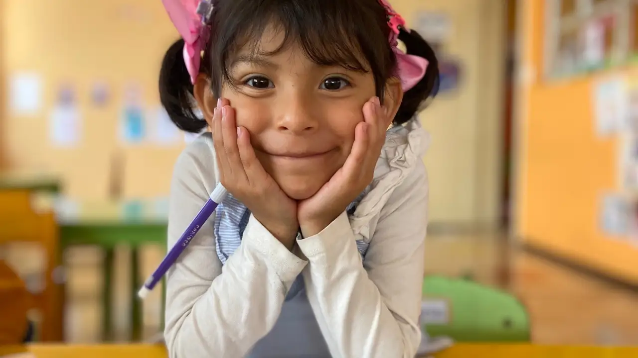 Niña pequeña sonriendo apoyada en sus manos dentro de una de las clases de Educación Inicial del Instituto INEPE.