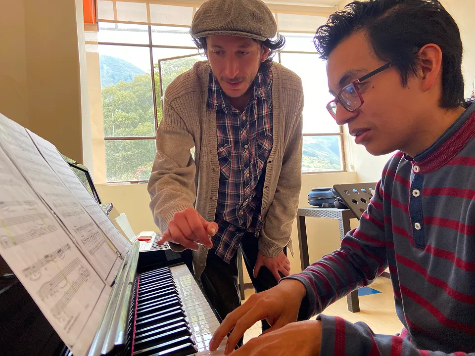 Docente enseñando a estudiante sobre clases de piano de forma práctica.